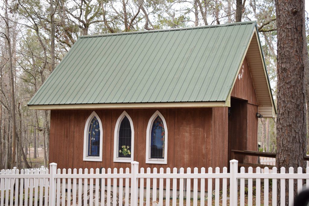 Small rustic wooden chapel with stained-glass windows, a green metal roof, and a white picket fence at Spirit of the Suwannee Music Park in Live Oak, Florida.