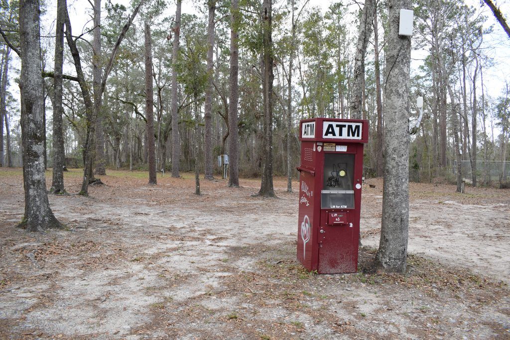 Weathered red ATM standing beside a tree in a wooded campground at Spirit of the Suwannee Music Park in Live Oak, Florida.