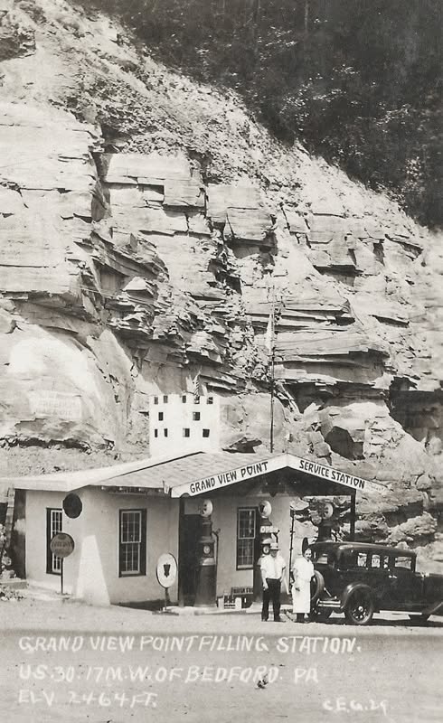 Historic black-and-white photograph of the Grand View Point Filling Station along Pennsylvania's Lincoln Highway, showing gasoline pumps, a vintage automobile, and people standing outside the small roadside building.