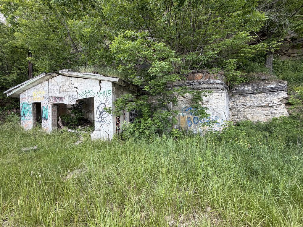 Modern photograph of the abandoned Grand View Point Filling Station near Mount Ararat, Pennsylvania, showing its crumbling concrete walls, graffiti-covered openings, and overgrown vegetation.