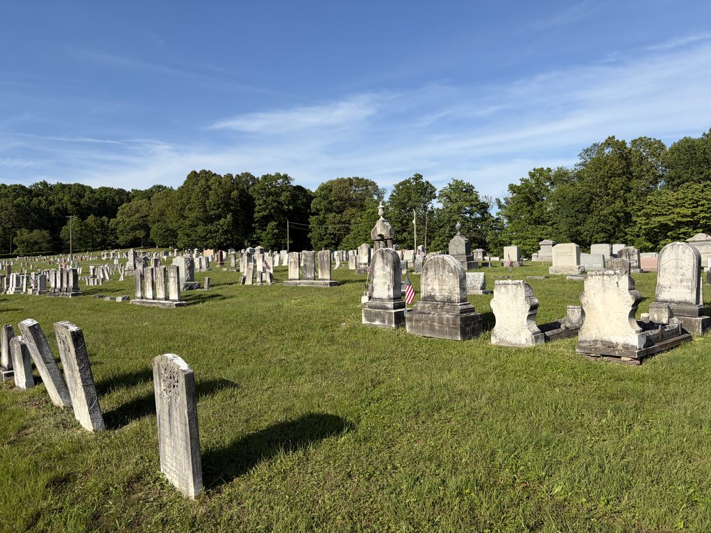 Historic gravestones and family monuments spread across the grassy Chestnut Ridge and Schellsburg Union Cemetery in Pennsylvania, including Schell family markers and American flags honoring veterans.