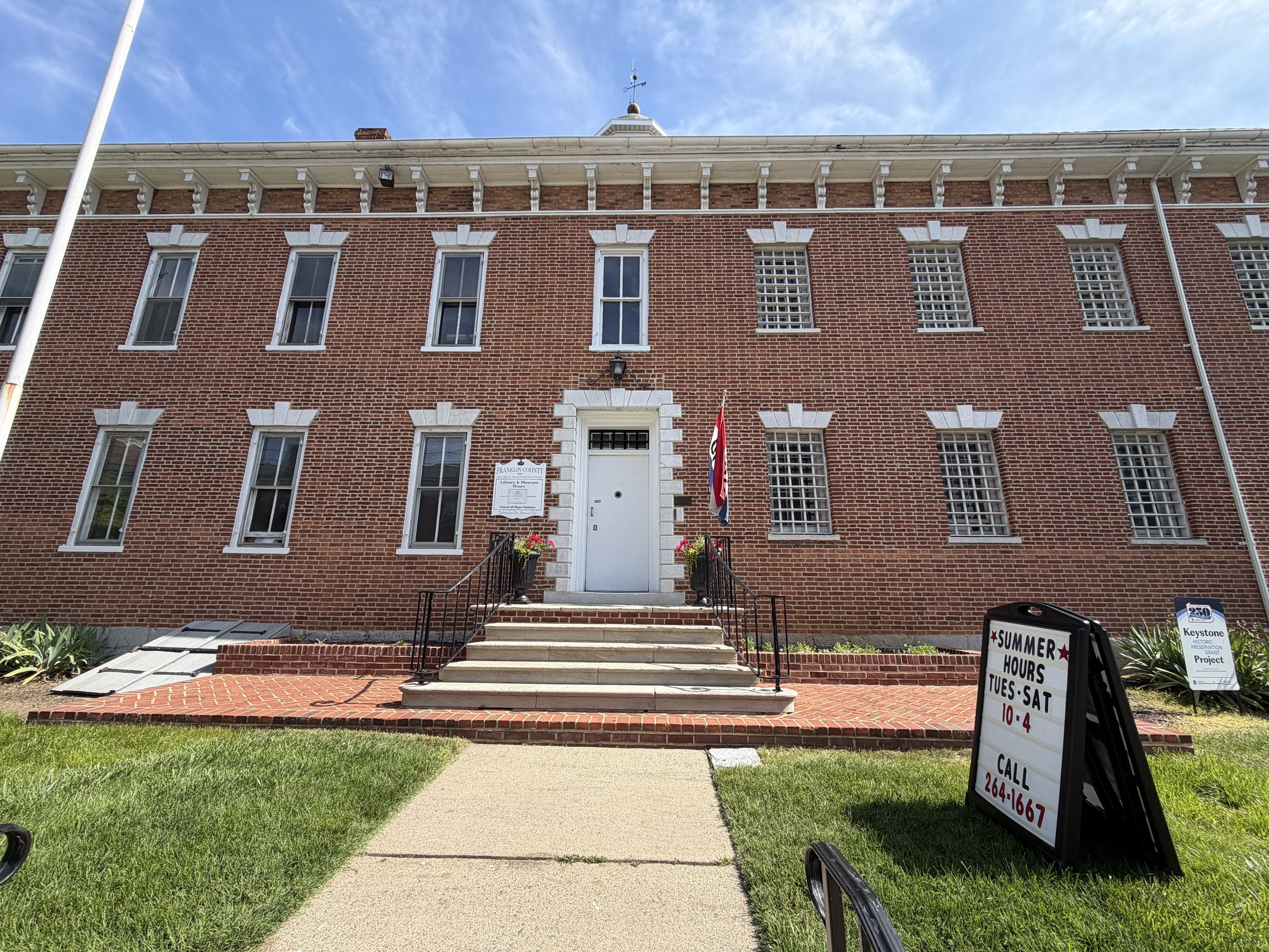 Front entrance of the historic Old Franklin County Jail in Chambersburg, Pennsylvania, featuring its red-brick exterior, barred windows, and central staircase.