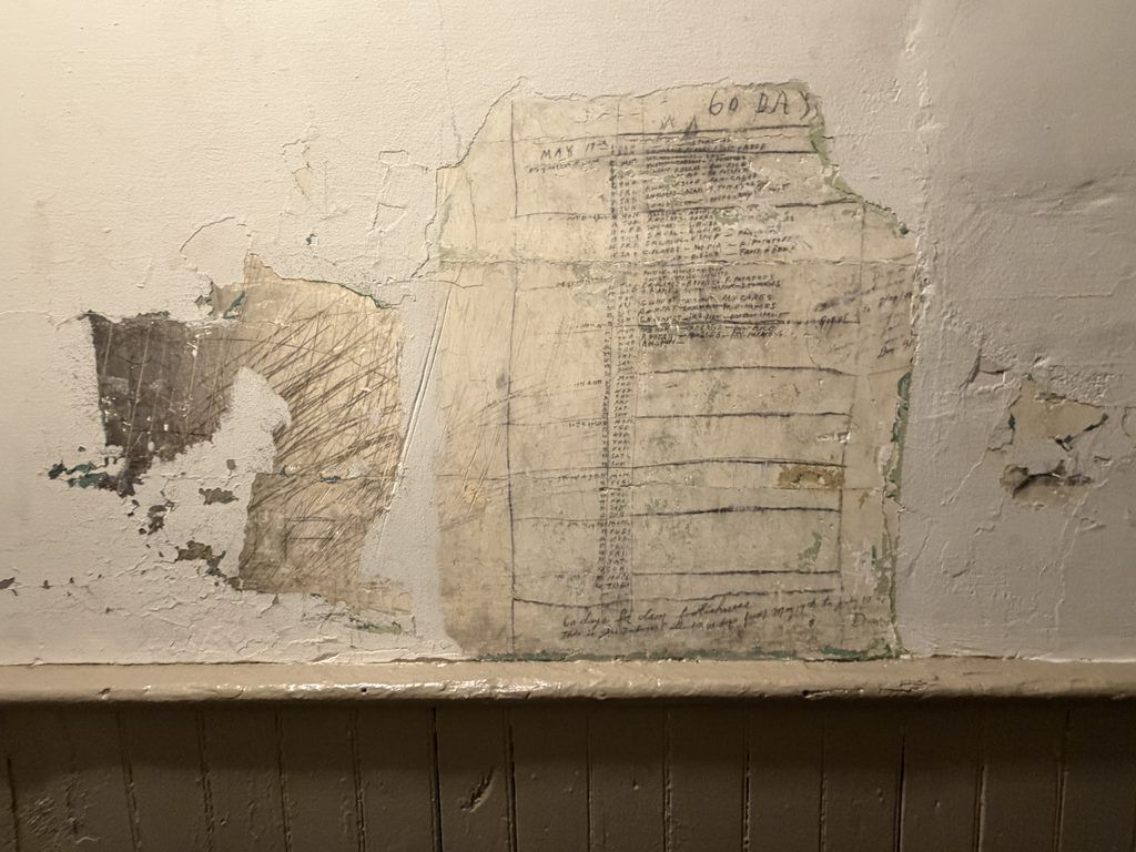 Faded handwritten prisoner inscriptions, tally marks, and a “60 DAYS” heading exposed beneath peeling paint on a cell wall inside the Old Franklin County Jail in Chambersburg, Pennsylvania.