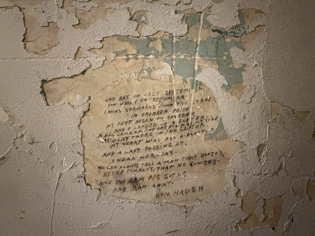 Handwritten poem signed Don Haugh about a drunken man and a pig, preserved beneath peeling paint on a historic cell wall at the Old Franklin County Jail in Chambersburg, Pennsylvania.