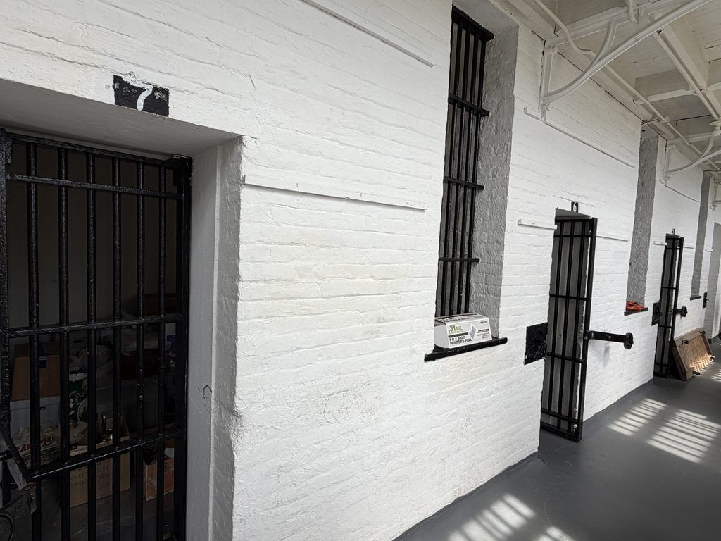 Interior cell block corridor at the Old Franklin County Jail in Chambersburg, Pennsylvania, featuring whitewashed brick walls, numbered iron-barred cell doors, and tall barred windows.