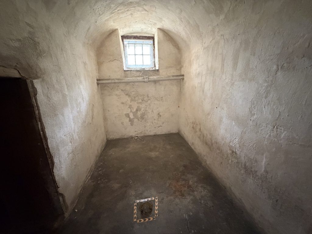 Underground dungeon cell at the Old Franklin County Jail in Chambersburg, Pennsylvania, featuring a vaulted ceiling, thick plaster walls, small barred window, and an iron shackle ring embedded in the floor.