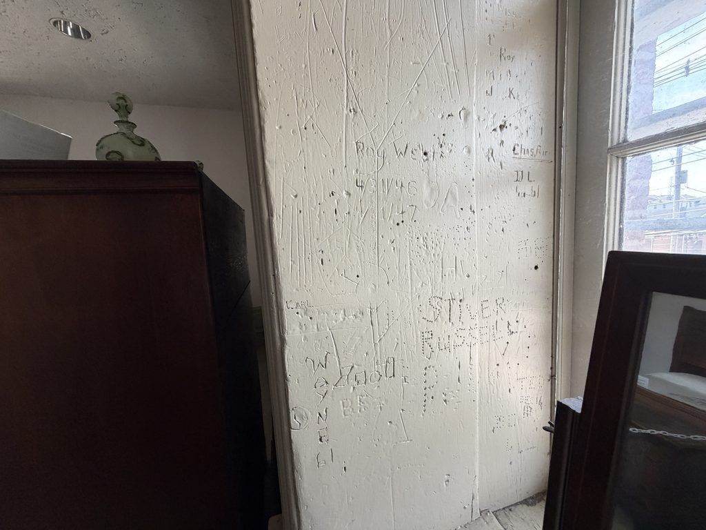 Names, initials, dates, and other inscriptions scratched into a white-painted wall beside a window inside the Old Franklin County Jail in Chambersburg, Pennsylvania.