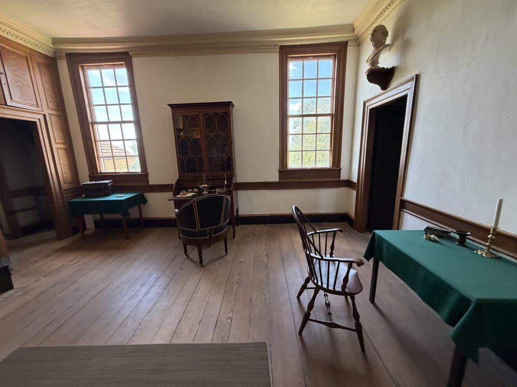 George Washington’s historic study at Mount Vernon in Virginia, featuring a wooden writing desk, antique chairs, bookcase, green-covered tables, and two tall windows.