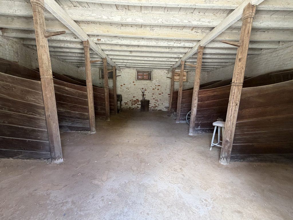 Interior of a historic stable at George Washington’s Mount Vernon Estate in Virginia, featuring wooden animal stalls, exposed timber beams, whitewashed brick walls, and a dirt floor.
