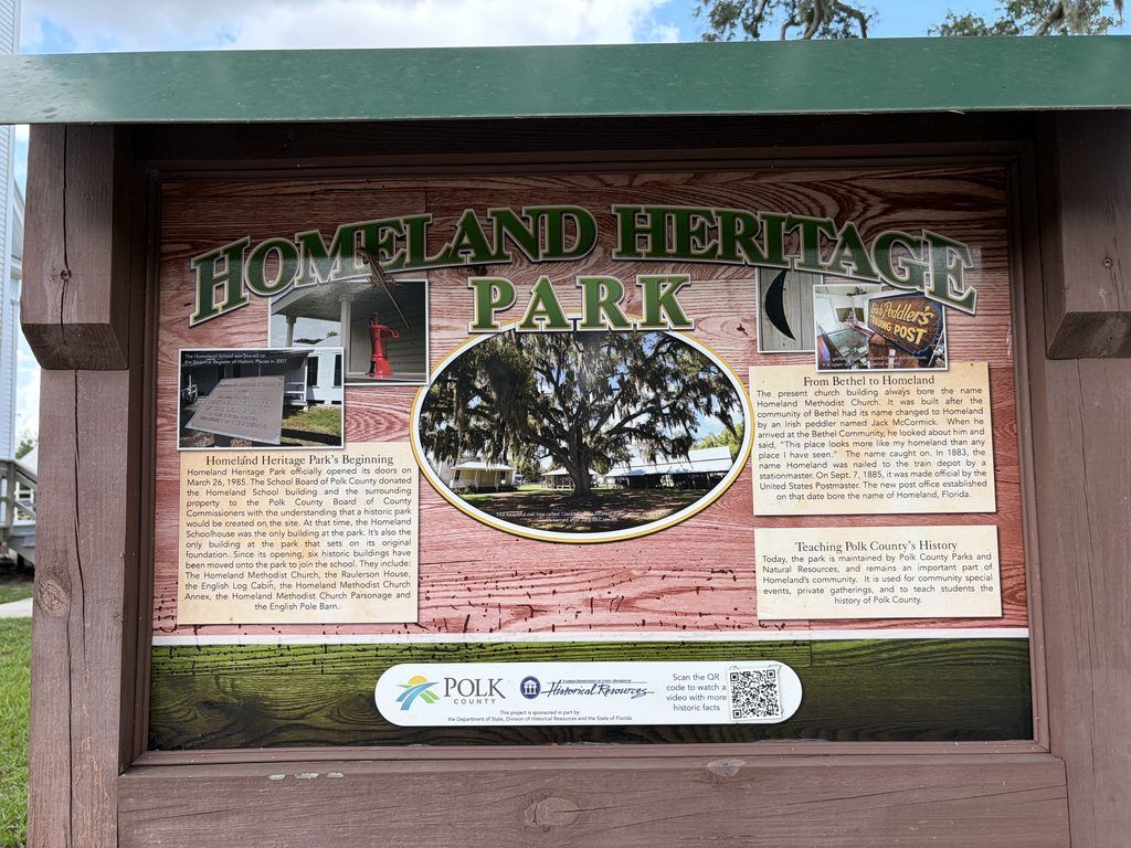 Wooden Homeland Heritage Park interpretive sign displaying historical photographs and information about the park's founding, pioneer buildings, and Homeland community in Polk County, Florida.
