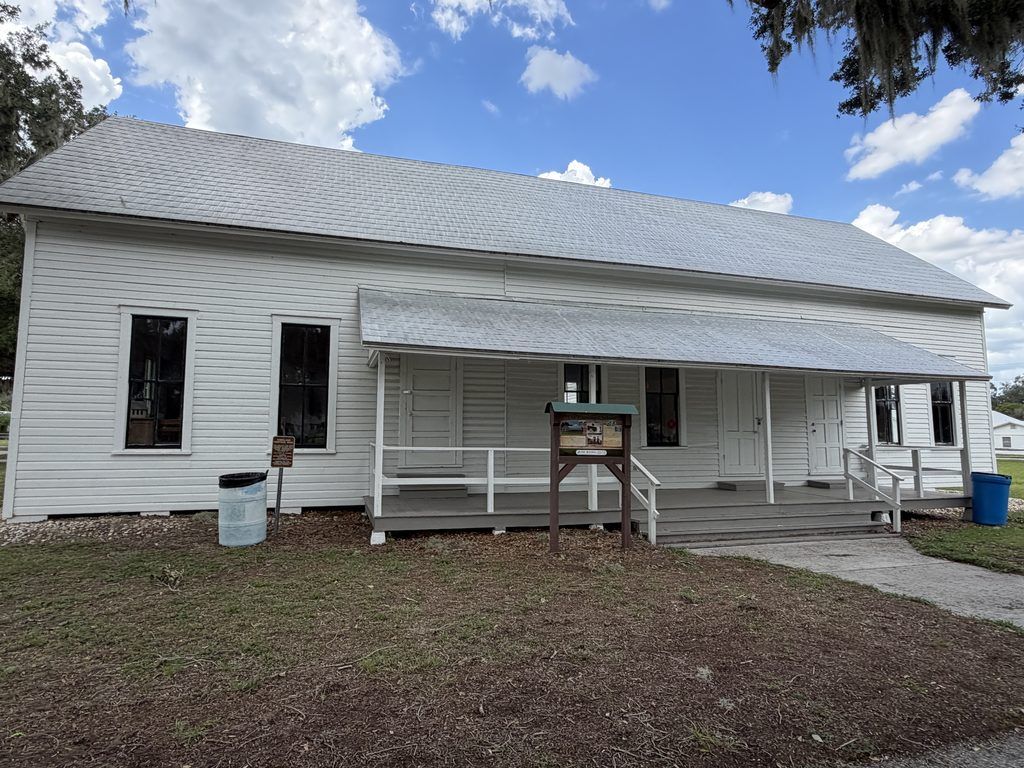 Historic white wooden Homeland School building at Homeland Heritage Park in Polk County, Florida, featuring a long covered porch, multiple classroom entrances, and an interpretive sign.