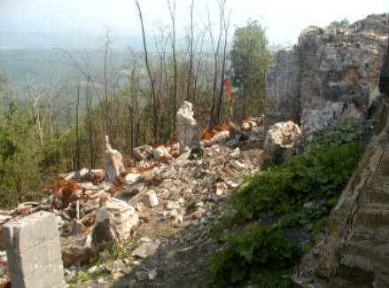 Scattered stone and concrete rubble on the mountainside at the former Grand View Ship Hotel site in Pennsylvania, with rocky cliffs and distant Allegheny Mountain views.